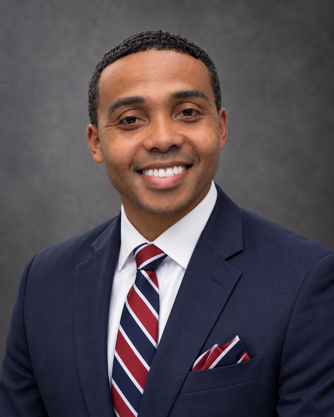 Portrait of Zonie Daniels IV in a navy blue suit with a red, white, and blue tie and coordinating pocket square